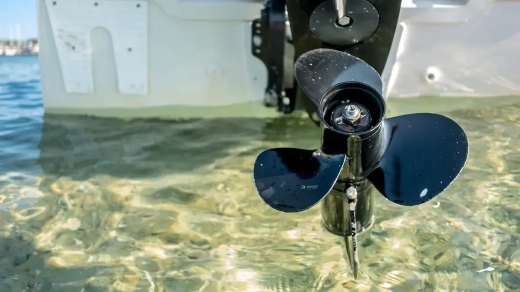 A black outboard boat propeller in clear shallow water over sand