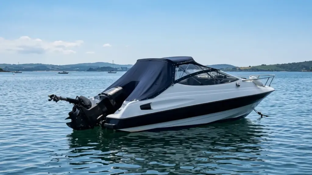A white powerboat with a dark canvas cover is anchored on water near a distant coastline with hills, suitable for an overview