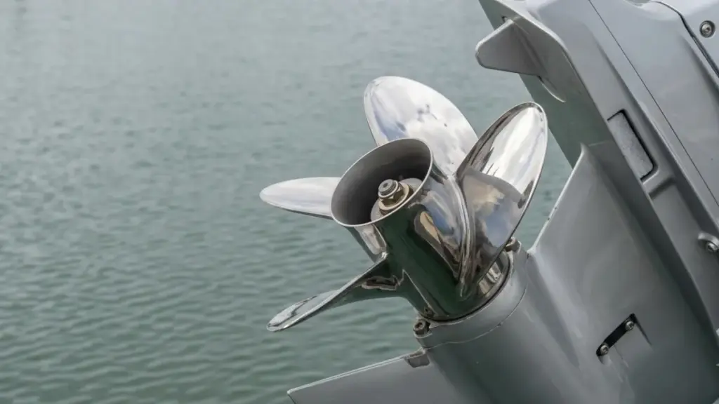 stainless outboard marine engine with a highly polished stainless steel four-blade propeller over calm green-grey water