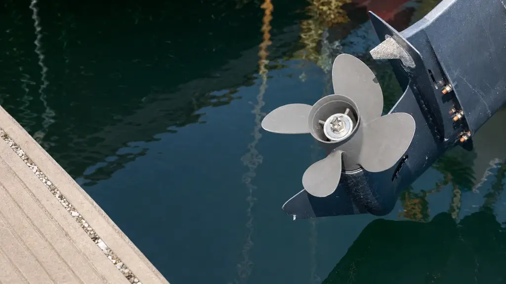 Black four-blade outboard propeller submerged in calm green water
