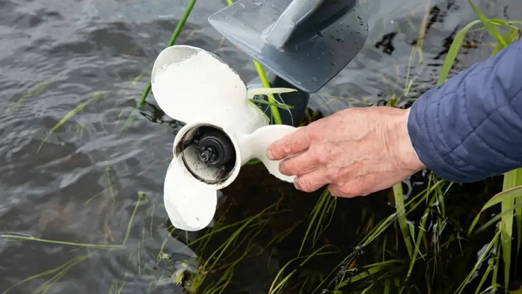 Hand touches a weed-entangled white boat propeller in water