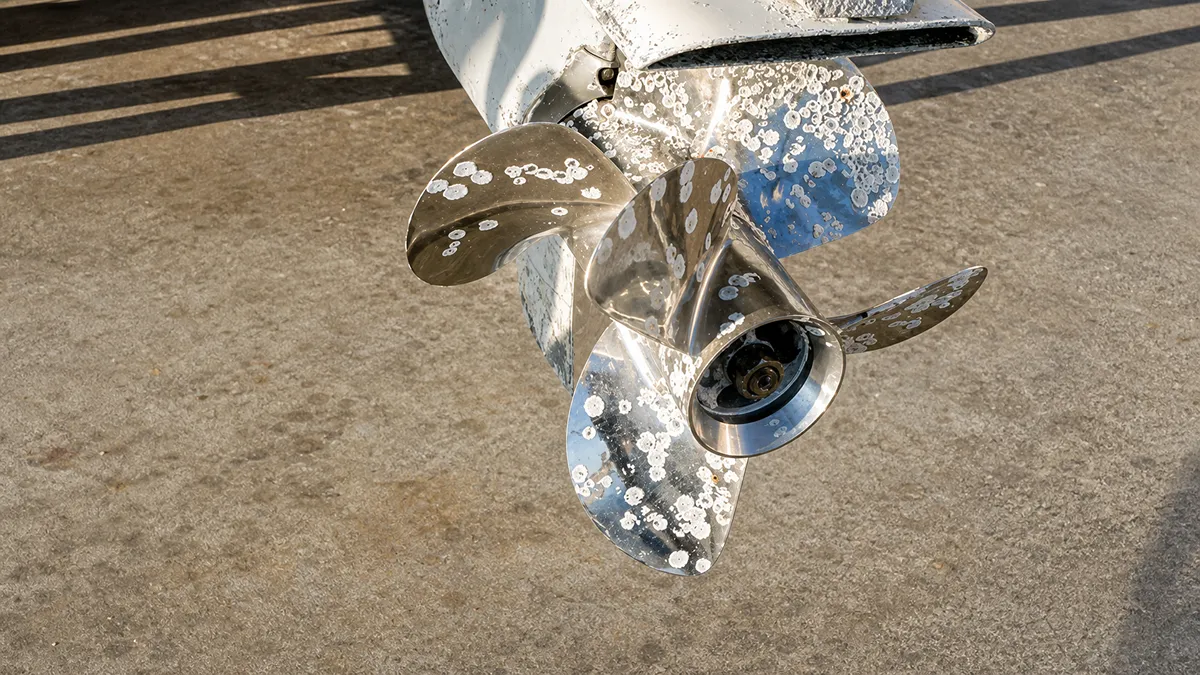 Metal boat propeller with corrosion spots, sunlit on concrete surface