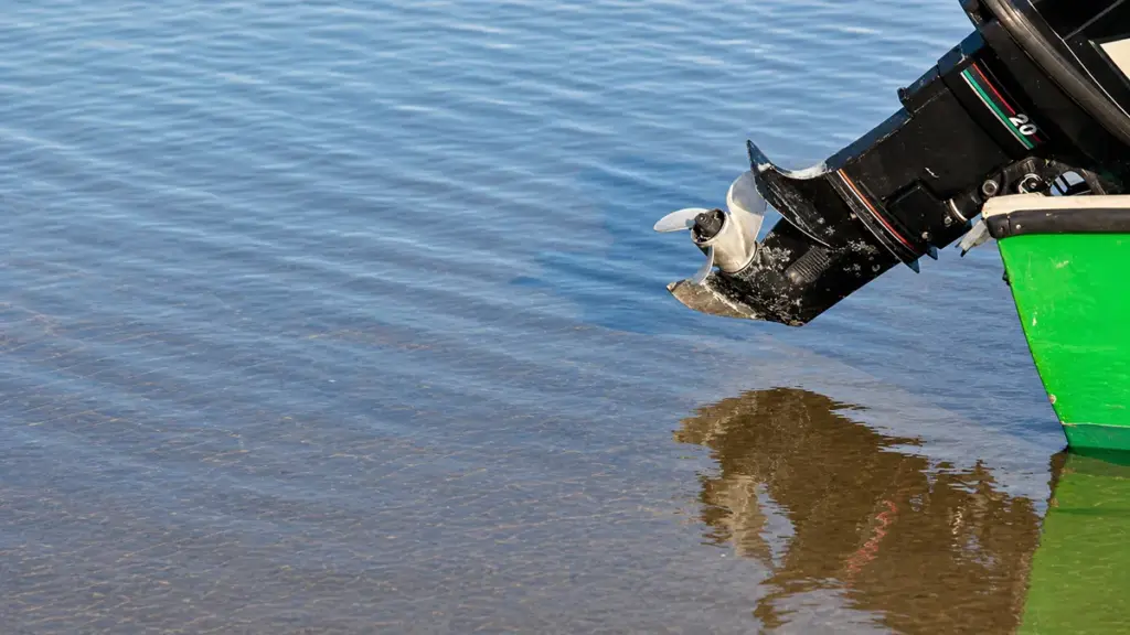 Outboard motor propeller partially submerged, reflecting on calm water