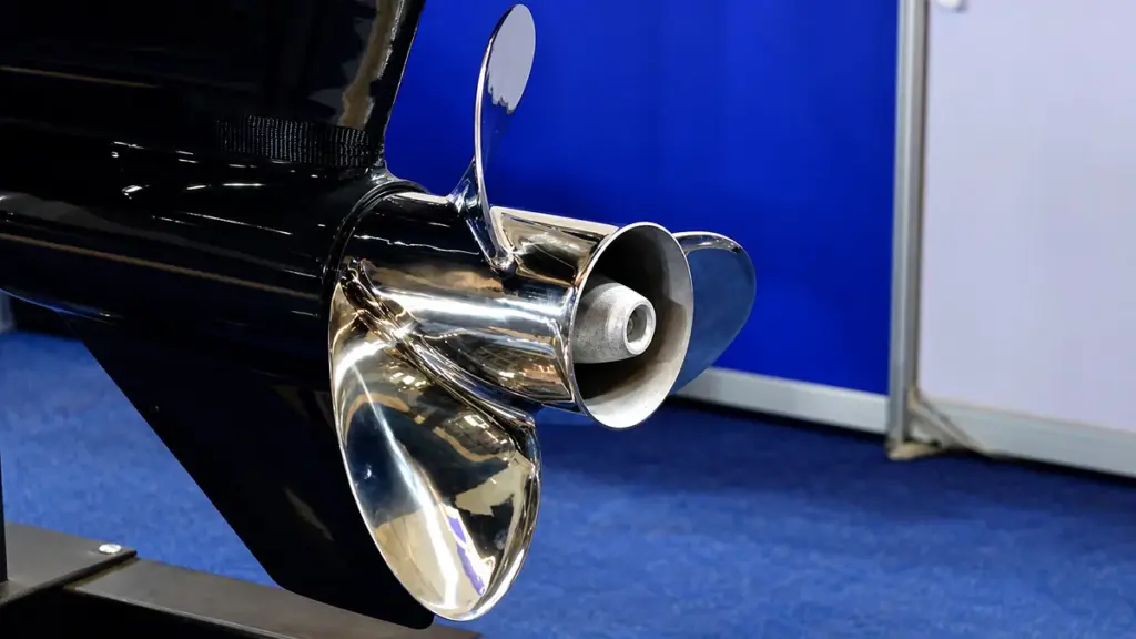 Polished metal propeller on black outboard motor, blue exhibition backdrop