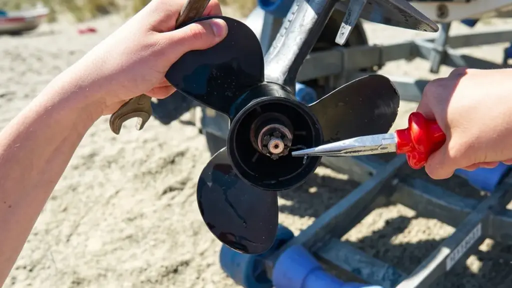 Using wrench and pliers to remove a boat propeller cotter pin on a sandy beach