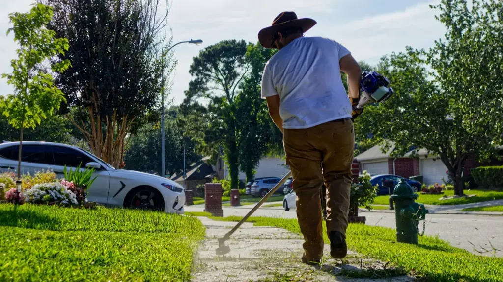 Man trimming grass along a suburban sidewalk using weed eater