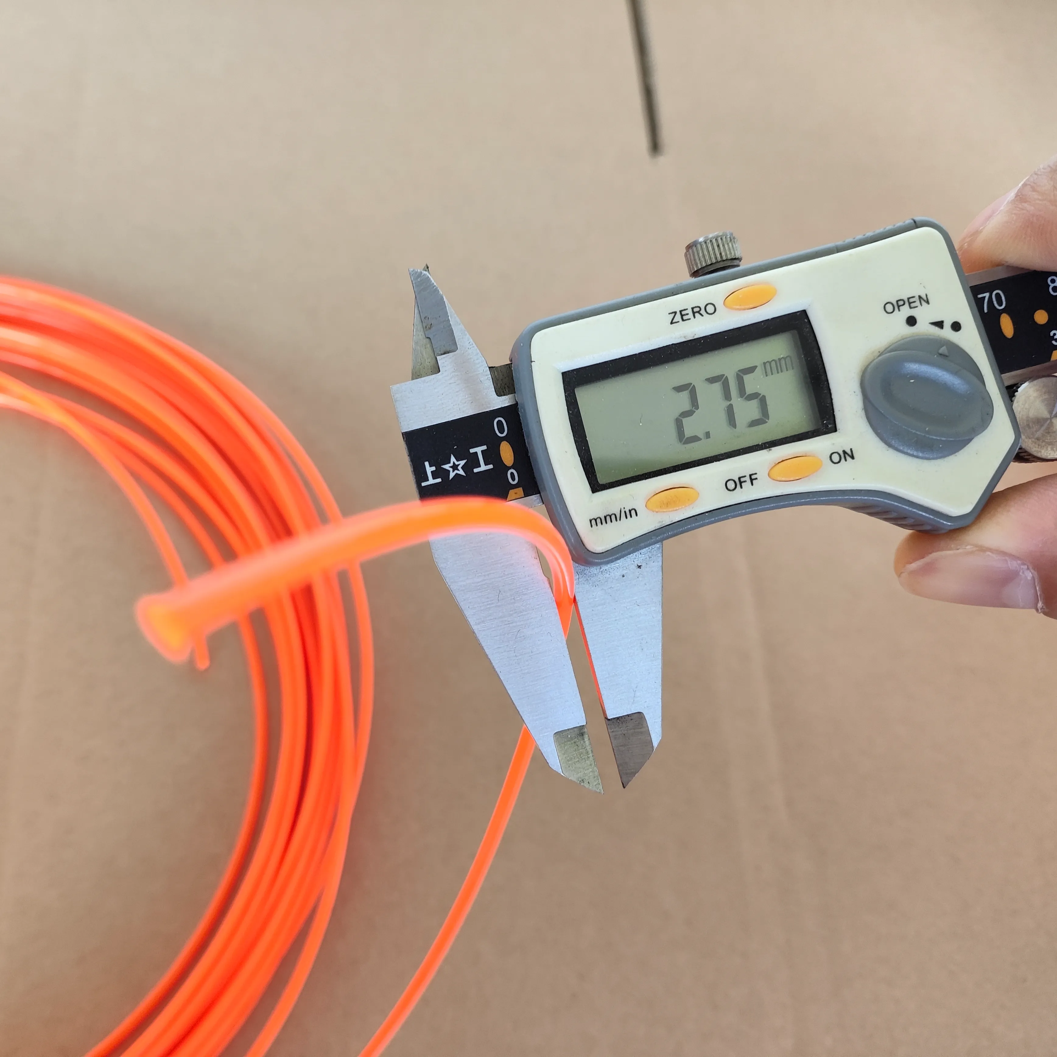 Coil of orange trimmer line being measured with a digital caliper showing a 2.75mm diameter.
